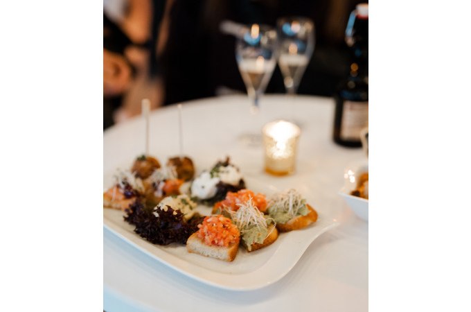 Vorspeisenteller mit Canapés auf weißem Tisch, zwei Gläser und Kerze im Hintergrund, romantische Atmosphäre., © Cool-Tours StattReisen