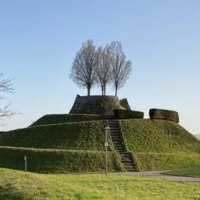 Eine grasbewachsene Erhebung mit einer Treppe und Bäumen auf der Spitze, umgeben von kahlen Bäumen, unter einem klaren blauen Himmel., © SMG