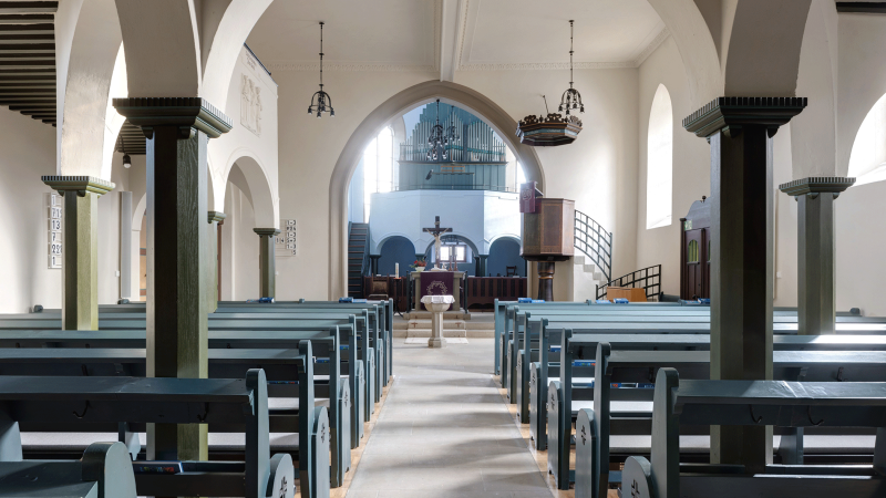Innenansicht der Kirche mit blauen Bänken, Altar, Kanzel und Orgel im Hintergrund. Helle Wände und große Bögen prägen den Raum., © Stadt Gaildorf