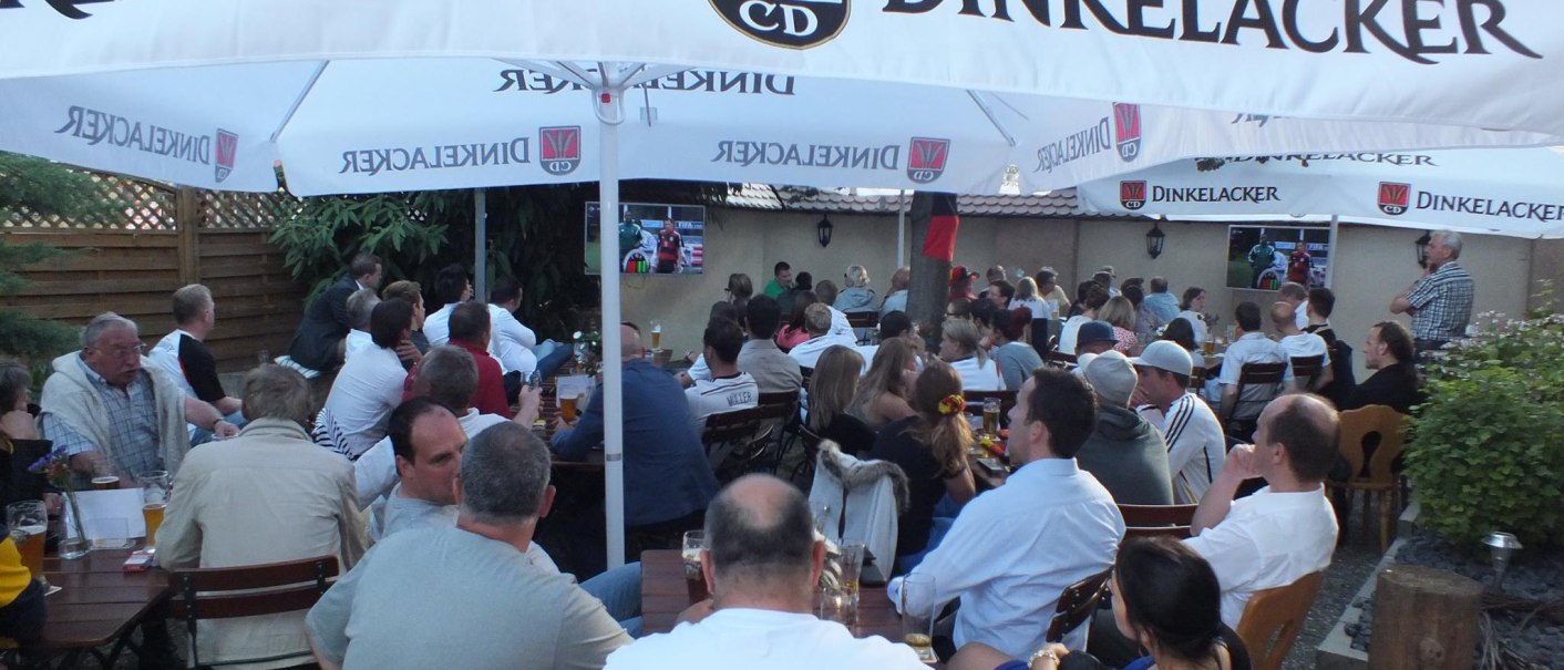 Menschen sitzen in einem Biergarten unter Dinkelacker-Sonnenschirmen und schauen auf einen Bildschirm., © Gasthof zum Bären