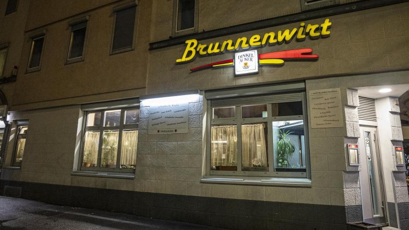 Das Restaurant Brunnenwirt bei Nacht, beleuchtet mit gelbem Schriftzug. Ein Mann steht an einem Tisch vor dem Eingang., &copy; SMG, Sarah Schmid