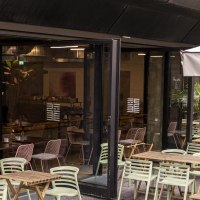 Außenbereich eines Cafés mit Holztischen und grünen Stühlen. Eine Markise trägt den Schriftzug 'Citizen Long'. Pflanzen dekorieren den Bereich., © SMG, Sarah Schmid
