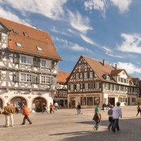 Der Marktplatz in Schorndorf zeigt malerische Fachwerkhäuser unter blauem Himmel. Menschen spazieren und verweilen auf dem Platz., © Oswald Der Marktplatz in Schorndorf zeigt malerische Fachwerkhäuser unter blauem Himmel. Menschen spazieren und verweilen auf dem Platz., © Oswald