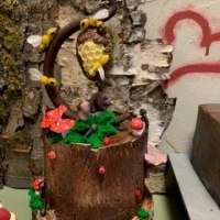Ein kunstvoll dekorierter Kuchen in Form eines Baumstamms mit Bienen, Pilzen und Moos. Im Hintergrund ist eine Birkenrinde und ein rotes Herz zu sehen., © Cafe Brunenberg