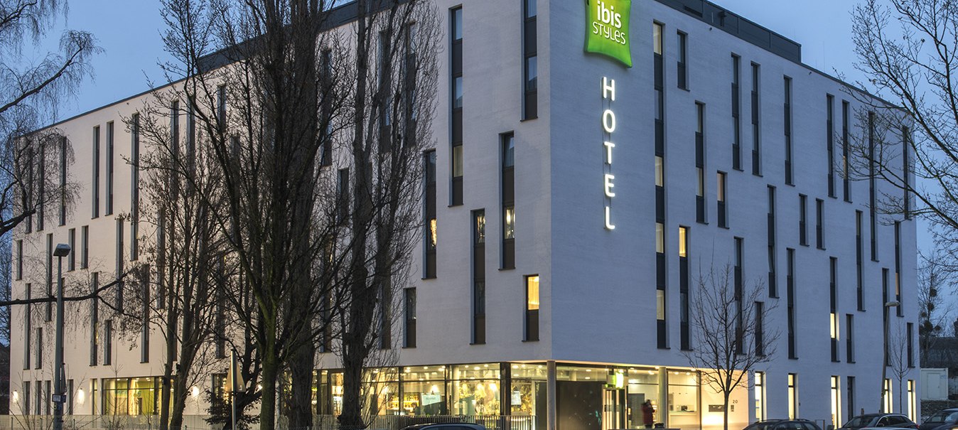 Modernes Hotelgebäude des ibis Styles Stuttgart Vaihingen bei Dämmerung, beleuchtet mit Autos auf der Straße davor., © ibis Styles Stuttgart Vaihingen