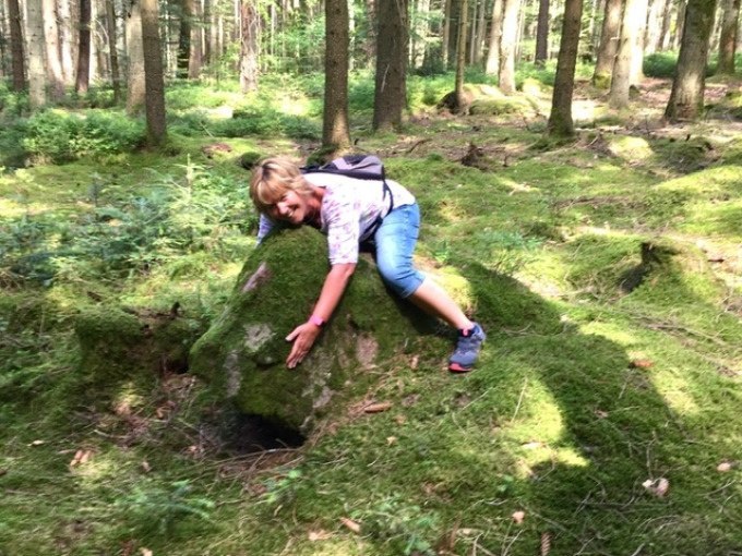 Eine Person umarmt einen moosbedeckten Stein in einem dichten, gr&uuml;nen Wald. Sie tr&auml;gt Freizeitkleidung und einen Rucksack., &copy; WTM GmbH Waiblingen