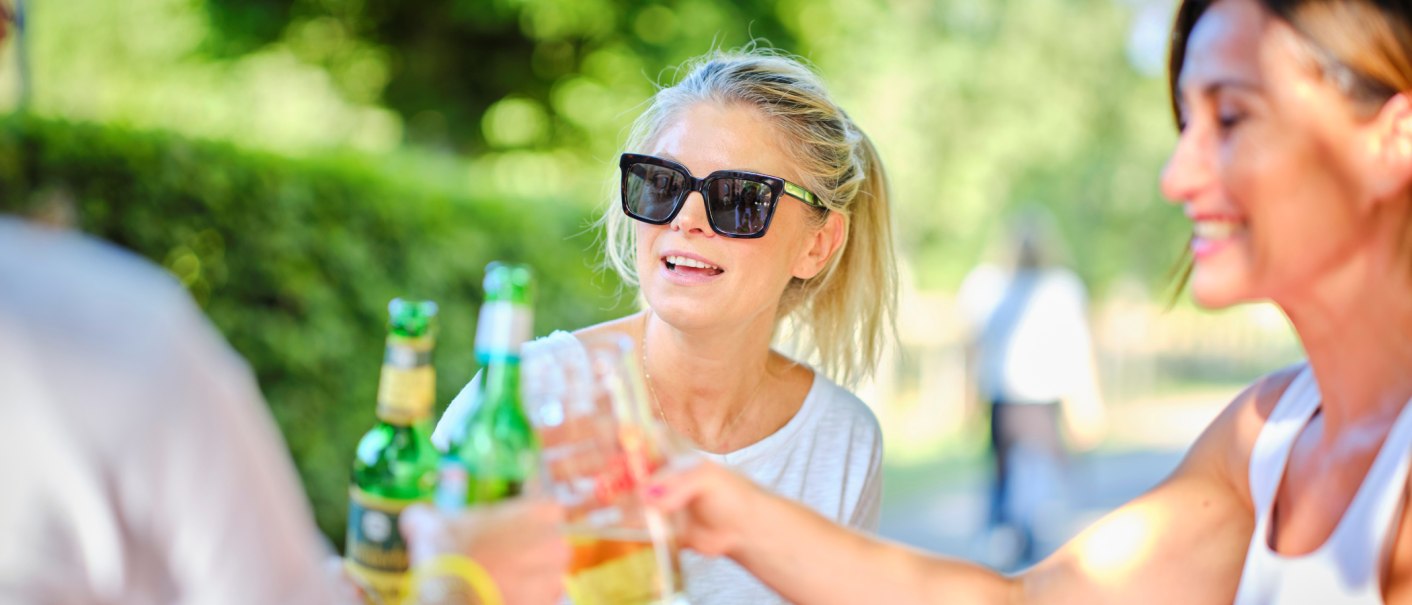 Drei Personen stoßen im Freien mit Getränken an. Eine Frau trägt eine Sonnenbrille und lächelt. Die Szene wirkt entspannt und sommerlich., © Katzenbacher Hof Drei Personen stoßen im Freien mit Getränken an. Eine Frau trägt eine Sonnenbrille und lächelt. Die Szene wirkt entspannt und sommerlich., © Katzenbacher Hof
