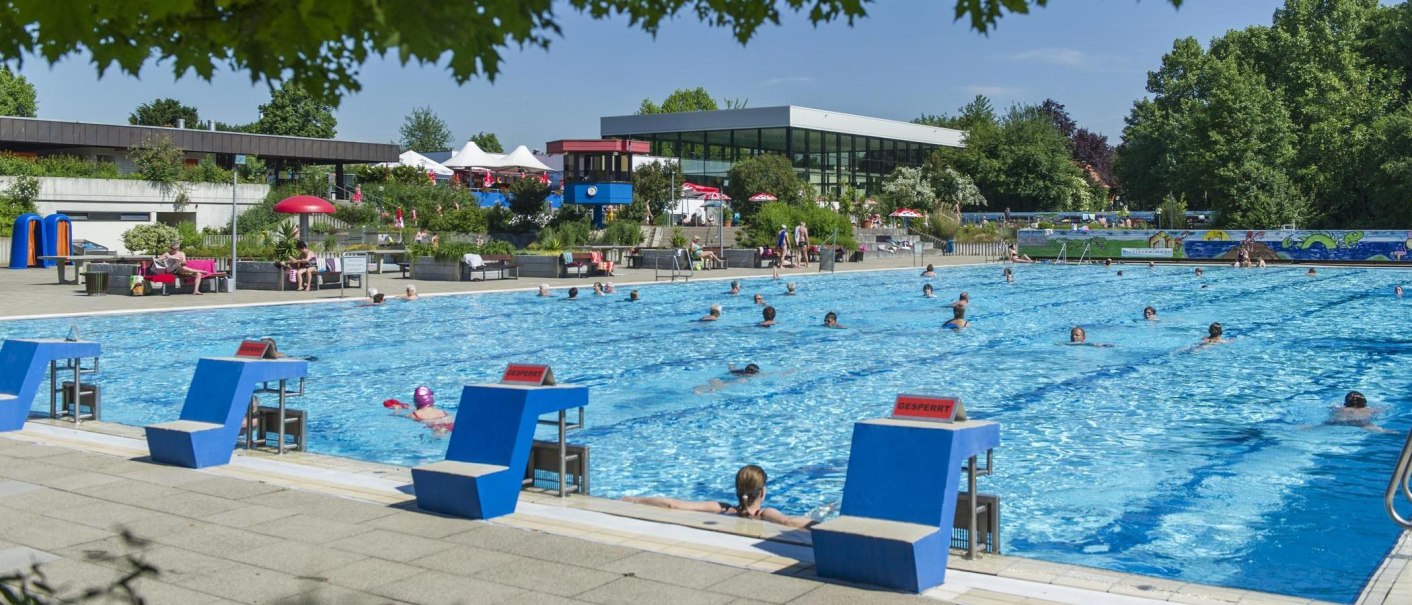 Ein Freibad mit vielen Schwimmern im Wasser. Im Hintergrund sind Liegestühle, Sonnenschirme und ein modernes Gebäude zu sehen., © Stadt Vaihingen an der Enz Ein Freibad mit vielen Schwimmern im Wasser. Im Hintergrund sind Liegestühle, Sonnenschirme und ein modernes Gebäude zu sehen., © Stadt Vaihingen an der Enz