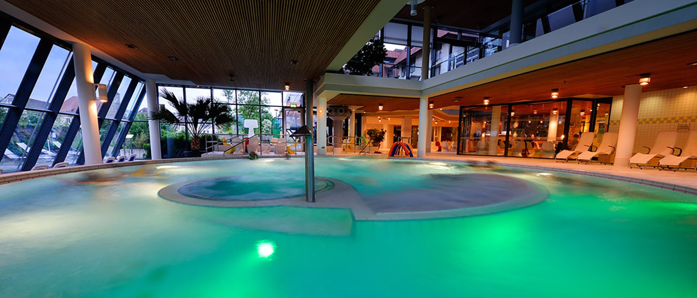 Modernes Schwimmbad mit beleuchtetem Wasser, großen Fenstern und Liegestühlen. Die Atmosphäre ist entspannt und einladend., © Ufuk Arslan