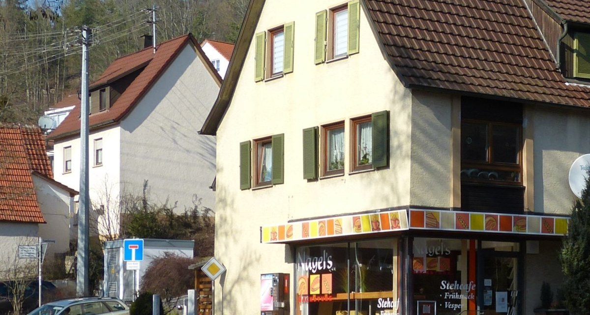 Ein Stehcafé in einem Eckgebäude mit gelber Fassade und grünen Fensterläden in Dätzingen. Im Hintergrund sind weitere Häuser und Bäume zu sehen., © Natur.Nah. Schönbuch & Heckengäu Ein Stehcafé in einem Eckgebäude mit gelber Fassade und grünen Fensterläden in Dätzingen. Im Hintergrund sind weitere Häuser und Bäume zu sehen., © Natur.Nah. Schönbuch & Heckengäu
