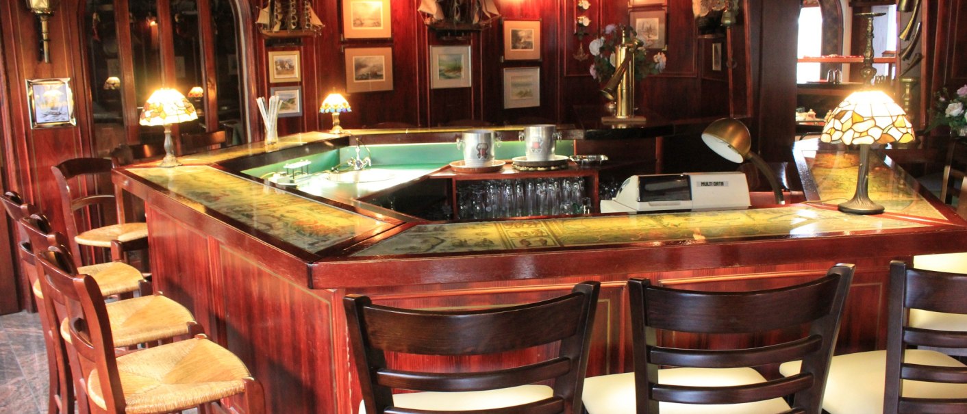 Eine gemütliche Hotelbar mit Holzmöbeln, Barhockern und dekorativen Lampen. An den Wänden hängen Bilder und maritime Dekorationen., © Hotel Spahr Eine gemütliche Hotelbar mit Holzmöbeln, Barhockern und dekorativen Lampen. An den Wänden hängen Bilder und maritime Dekorationen., © Hotel Spahr