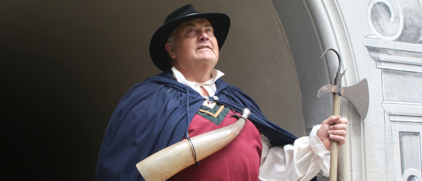 Ein Nachtwächter in historischer Kleidung mit Horn und Hellebarde vor einem Torbogen in Gaildorf., © Petra Natzkowski Ein Nachtwächter in historischer Kleidung mit Horn und Hellebarde vor einem Torbogen in Gaildorf., © Petra Natzkowski
