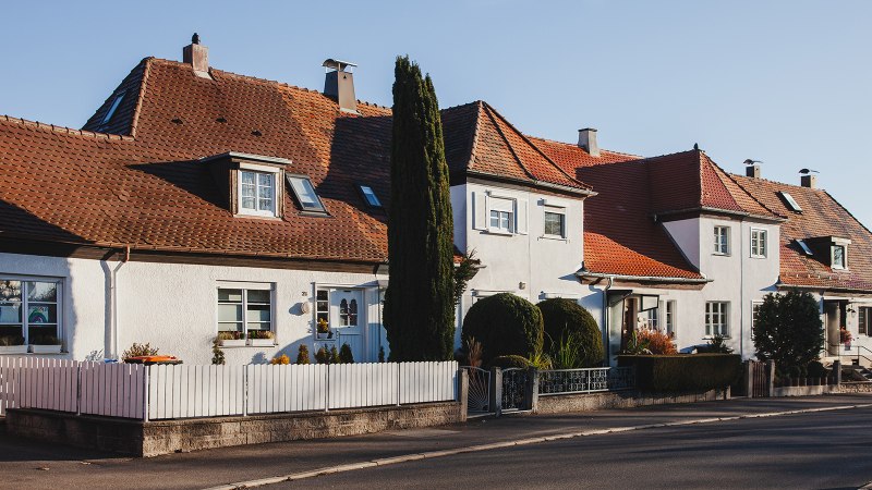 Reihenhäuser mit roten Ziegeldächern und weißen Fassaden in einer ruhigen Wohnsiedlung bei Sonnenschein., © benjaminknoblauch.de