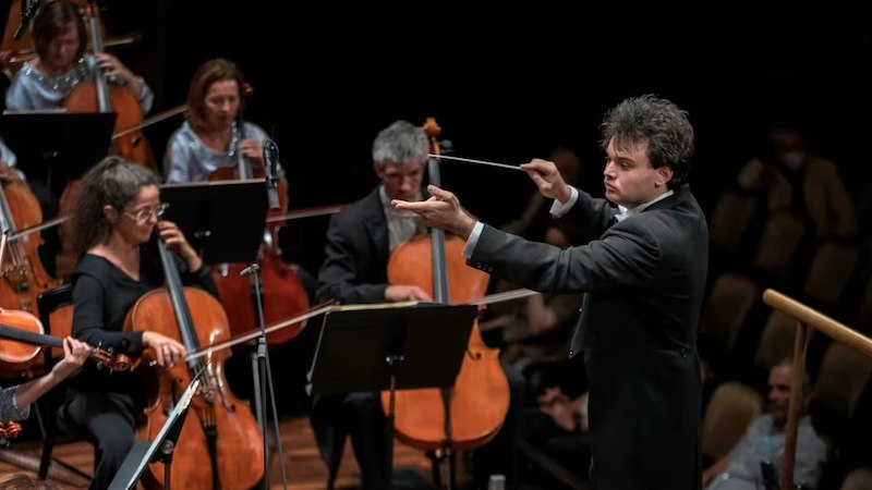 Ein Dirigent führt ein Orchester mit Streichinstrumenten auf einer Bühne. Die Musiker konzentrieren sich auf ihre Instrumente., © Kammerkonzerte Schwäbisch Hall e.V.