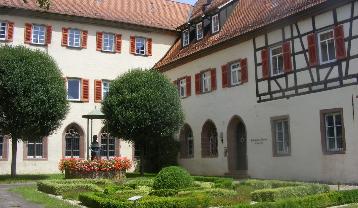 Historisches Gebäude mit Fachwerk und rotem Dach in Bad Mergentheim. Gepflegter Garten mit Brunnen und Blumen im Vordergrund., © Natur.Nah. Schönbuch & Heckengäu Historisches Gebäude mit Fachwerk und rotem Dach in Bad Mergentheim. Gepflegter Garten mit Brunnen und Blumen im Vordergrund., © Natur.Nah. Schönbuch & Heckengäu