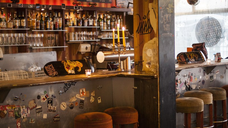 Eine gemütliche Bar mit Skateboard-Dekor auf der Theke, Kerzenleuchter und Barhockern. Im Hintergrund sind Flaschen und Gläser zu sehen., © Mata Hari, Stuttgart Eine gemütliche Bar mit Skateboard-Dekor auf der Theke, Kerzenleuchter und Barhockern. Im Hintergrund sind Flaschen und Gläser zu sehen., © Mata Hari, Stuttgart