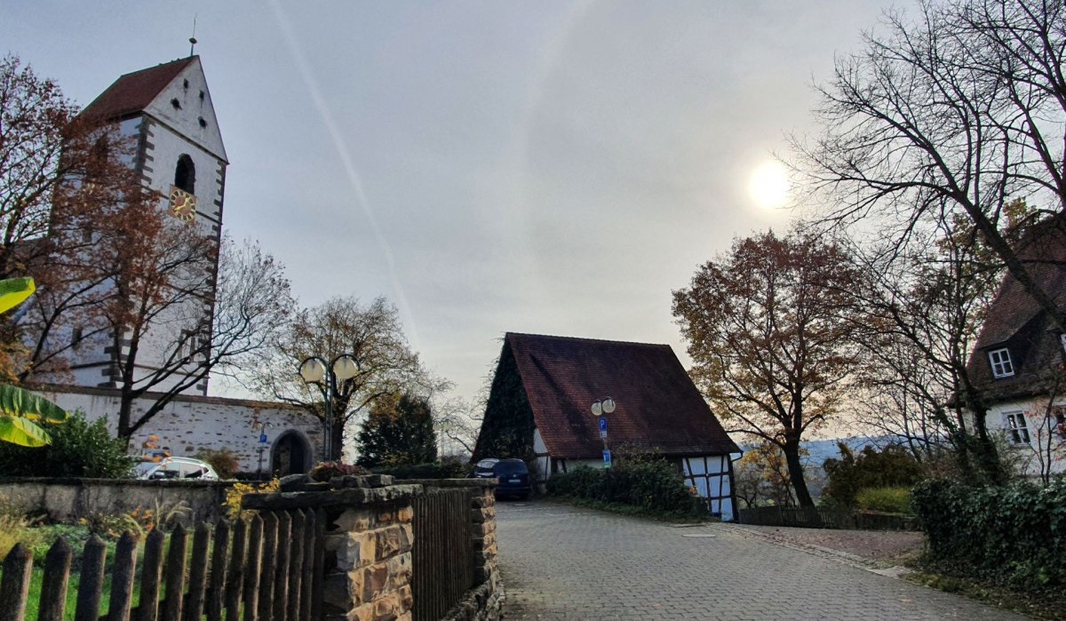 Herbstliche Szene in Kirchberg mit einer Kirche, einem Fachwerkhaus und kahlen Bäumen unter einem bewölkten Himmel., © Kulturamt Plochingen