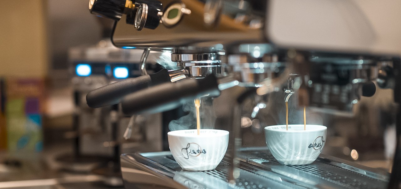Eine Espressomaschine brüht frischen Kaffee in zwei weiße Tassen. Der Kaffee fließt in einem dünnen Strahl in die Tassen., © Café Justus, Stuttgart