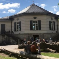 Das Bärenschlössle in Stuttgart, umgeben von Bäumen, mit Menschen, die draußen bei sonnigem Wetter entspannen und spielen., © SMG