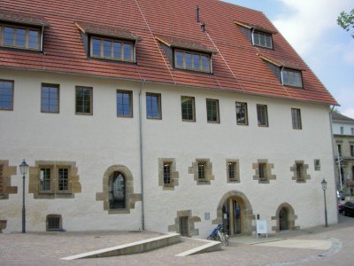 Ein historisches Geb&auml;ude mit roten Dachziegeln und mehreren Fenstern. Vor dem Geb&auml;ude steht ein Fahrrad.