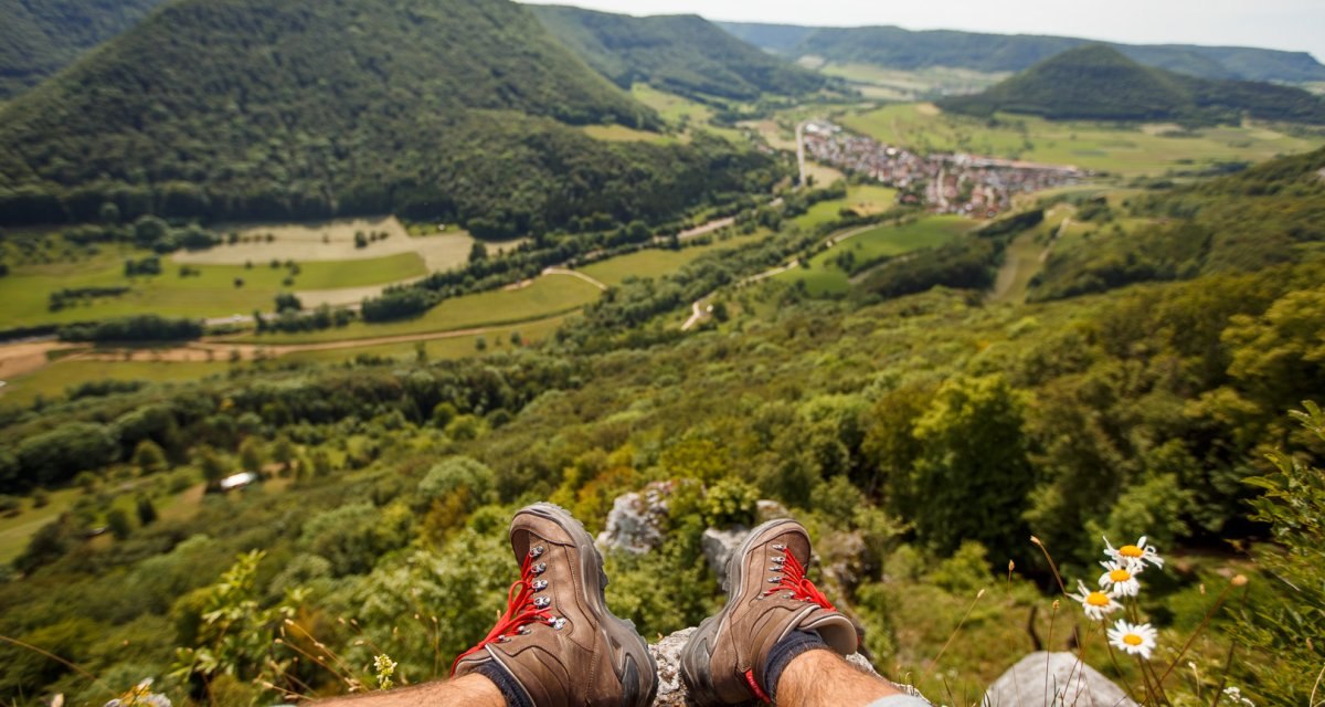 Panoramablick ins Obere Filstal, im Vordergrund Wanderstiefel und Gänseblümchen, im Hintergrund grüne Hügel und ein Dorf., © Distretto di Göppingen Panoramablick ins Obere Filstal, im Vordergrund Wanderstiefel und Gänseblümchen, im Hintergrund grüne Hügel und ein Dorf., © Distretto di Göppingen
