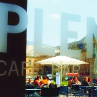 Menschen sitzen im Au&szlig;enbereich eines Caf&eacute;s unter Sonnenschirmen. Im Hintergrund sind historische Geb&auml;ude zu sehen., &copy; SMG