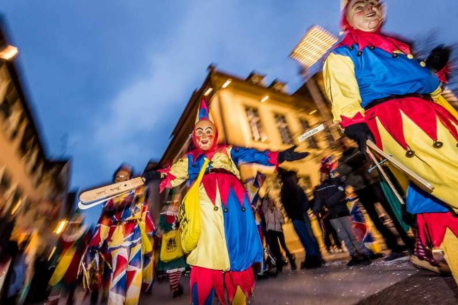 Bunte Narren in farbenfrohen Kostümen und Masken beim Göppinger Nachtnarrensprung, umgeben von Zuschauern in einer abendlichen Straßenszene.