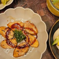 Ein Teller mit veganen Teigtaschen in So&szlig;e, ein Bao Bun mit Gem&uuml;se und ein Getr&auml;nk mit Eisw&uuml;rfeln auf einem Holztisch., &copy; SMG