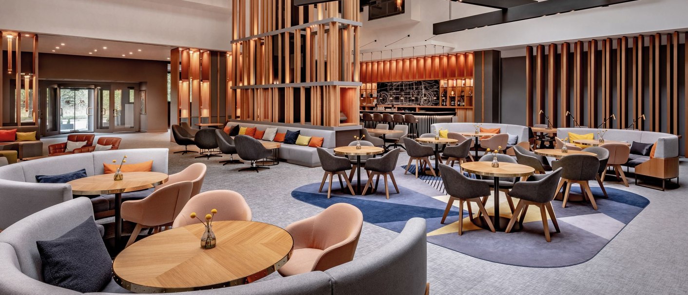 Moderne Lobby mit eleganten Sitzgruppen, Holzelementen und einer Bar im Hintergrund. Die Einrichtung wirkt einladend und stilvoll., © Stuttgart Marriott Hotel Sindelfingen