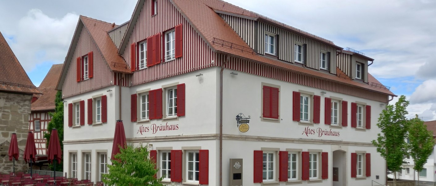 mehrstöckiges Gebäude mit hell verputzter Fassade und rötlich-braun holzverkleidetem Dachgeschoss, die zahlreichen weißgerahmten Sprossenfnster haben rot lackierte Klappläden, © Petra Natzkowski mehrstöckiges Gebäude mit hell verputzter Fassade und rötlich-braun holzverkleidetem Dachgeschoss, die zahlreichen weißgerahmten Sprossenfnster haben rot lackierte Klappläden, © Petra Natzkowski
