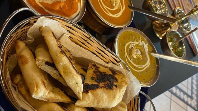 Drei Schalen mit indischen Currys und ein Korb mit Naan-Brot auf einem Tisch in einem Restaurant., © Taj Mahal Bad Urach