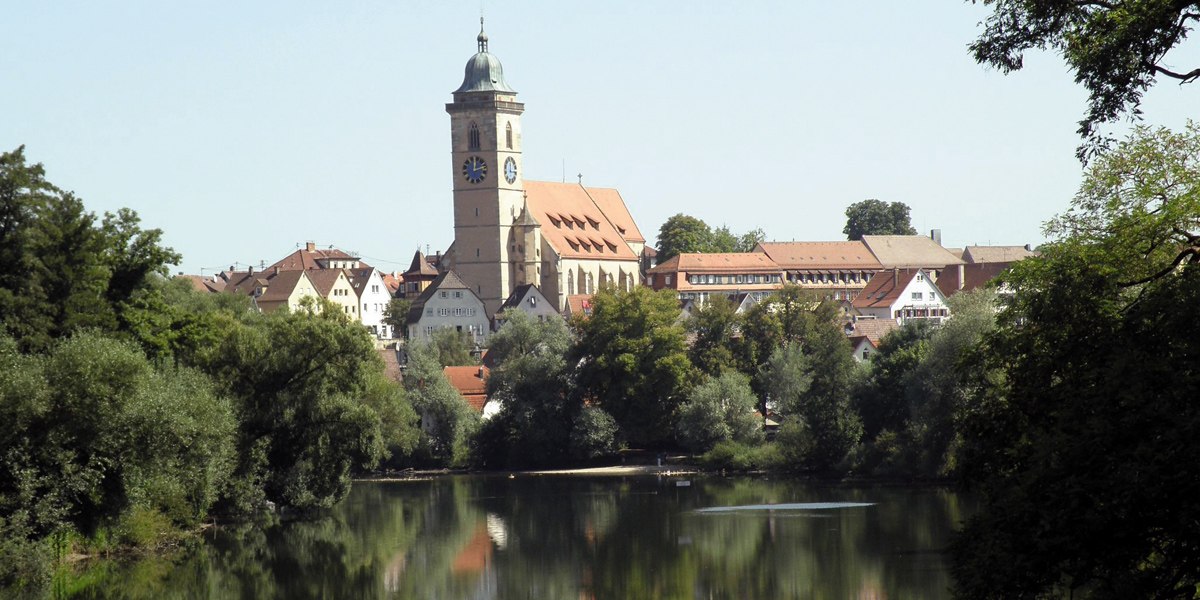 Die Stadtkirche St. Laurentius in Nürtingen erhebt sich über die Stadt, umgeben von Bäumen und einem ruhigen Fluss im Vordergrund., © Stuttgart-Marketing GmbH