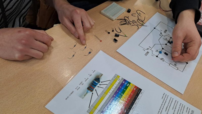 Zwei Personen arbeiten an einem Schaltkreis mit elektronischen Bauteilen und einem Schaltplan auf einem Tisch., © ©makerspace
