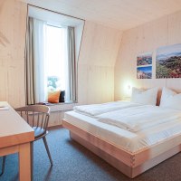 Modernes Hotelzimmer mit Holzw&auml;nden, Doppelbett, Schreibtisch und Fensterbank. An der Wand h&auml;ngen Bilder von Landschaften., &copy; Hotel Bergamo