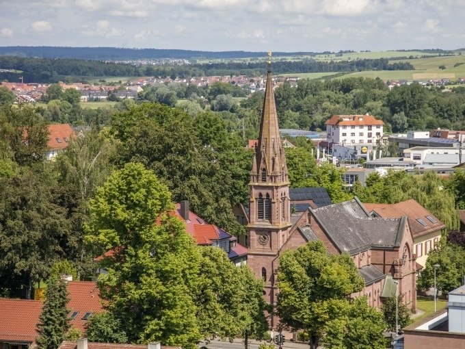 Eine Kirche mit hohem Turm inmitten von B&auml;umen und Geb&auml;uden, umgeben von einer l&auml;ndlichen Landschaft unter blauem Himmel., &copy; Stadtverwaltung Weil der Stadt