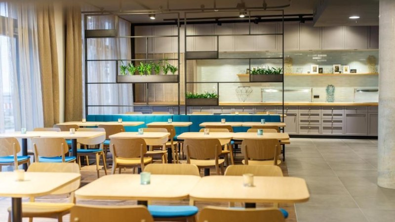 Moderner Speisesaal mit Holztischen und blauen Stühlen. Im Hintergrund sind Pflanzen und Regale zu sehen. Helle, einladende Atmosphäre., © Arthotel ANA Momentum Moderner Speisesaal mit Holztischen und blauen Stühlen. Im Hintergrund sind Pflanzen und Regale zu sehen. Helle, einladende Atmosphäre., © Arthotel ANA Momentum