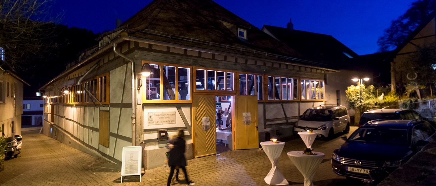 Fachwerkgebäude bei Nacht, beleuchtete Fenster, geöffnete Türen. Davor stehen Stehtische mit weißen Tischdecken. Personen und Autos sind zu sehen., © Steilwerk Rohracker Fachwerkgebäude bei Nacht, beleuchtete Fenster, geöffnete Türen. Davor stehen Stehtische mit weißen Tischdecken. Personen und Autos sind zu sehen., © Steilwerk Rohracker