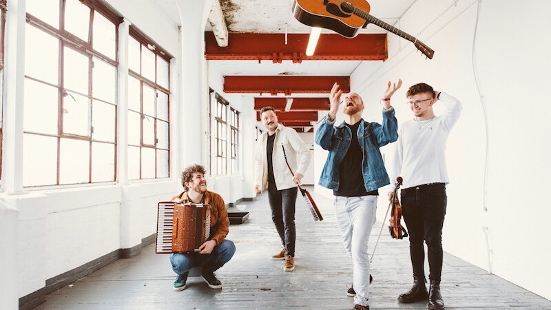 Vier M&auml;nner in einem hellen Raum, einer wirft eine Gitarre in die Luft. Die anderen halten Instrumente und l&auml;cheln. Der Raum hat gro&szlig;e Fenster und rote Deckenbalken., &copy; Stadt Leinfelden-Echterdingen, Kulturamt