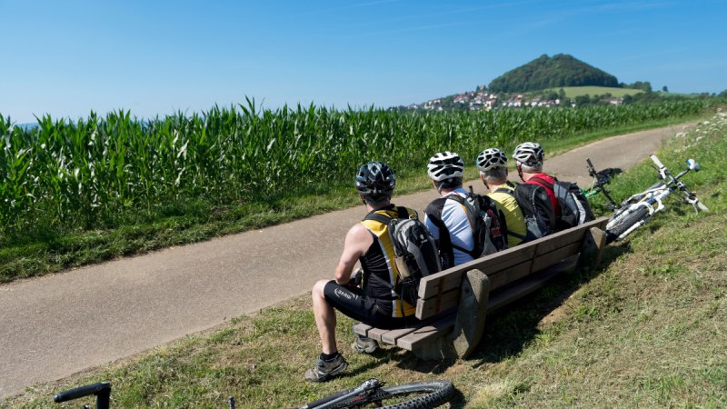 Drei Radfahrer mit Helmen sitzen auf einer Bank am Wegesrand, Fahrräder liegen daneben. Im Hintergrund ist der Hohenstaufen zu sehen., © Landkreis Göppingen Drei Radfahrer mit Helmen sitzen auf einer Bank am Wegesrand, Fahrräder liegen daneben. Im Hintergrund ist der Hohenstaufen zu sehen., © Landkreis Göppingen