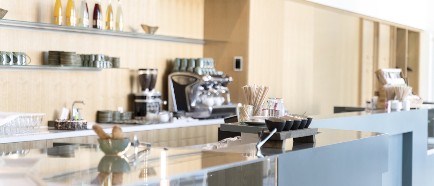 Modernes Café mit glänzender Theke, Kaffeemaschine und Regalen mit Tassen und Flaschen an der Wand., © Dominique Brewing