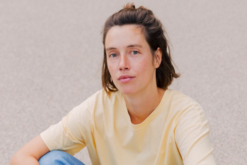 Eine Frau mit braunen Haaren in einem gelben T-Shirt sitzt vor einem grauen Hintergrund., © Kulturamt der Stadt Esslingen am Neckar