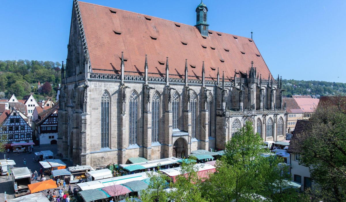 Das Heilig Kreuz Münster mit gotischer Architektur, umgeben von Marktständen und Fachwerkhäusern, unter einem klaren blauen Himmel., © Hostrup Fotografie Das Heilig Kreuz Münster mit gotischer Architektur, umgeben von Marktständen und Fachwerkhäusern, unter einem klaren blauen Himmel., © Hostrup Fotografie