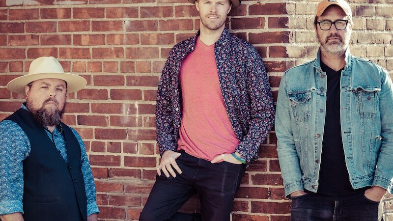 Drei M&auml;nner posieren l&auml;ssig vor einer Backsteinmauer mit dem Schriftzug 'Work is love made visible'., &copy; Mauerwerk GmbH