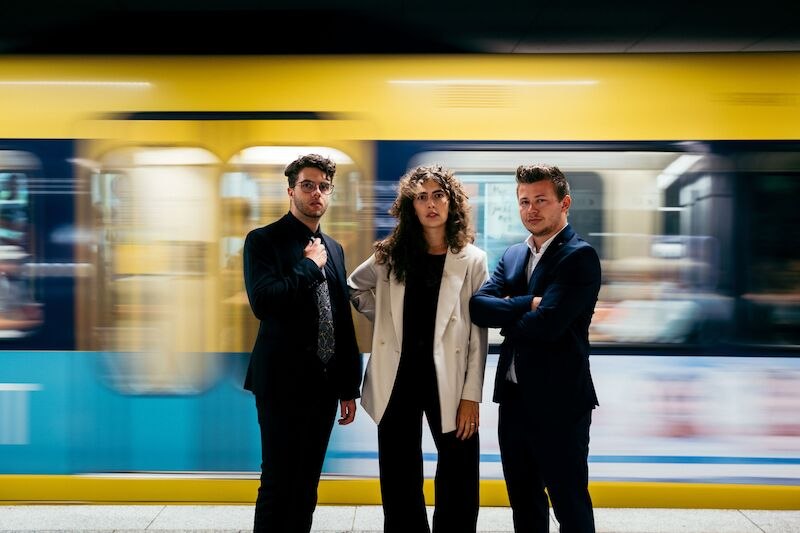 Drei Personen in eleganter Kleidung stehen vor einer vorbeifahrenden gelben U-Bahn. Sie blicken ernst in die Kamera., © Interessengemeinschaft Kultur Sindelfingen / Böblingen e.V.