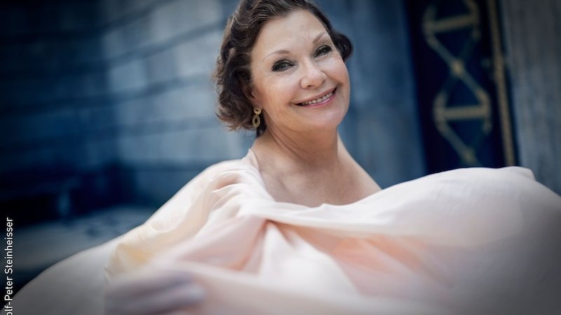 Eine Frau in einem fließenden, eleganten Kleid lächelt freundlich in die Kamera. Der Hintergrund ist unscharf und zeigt eine Steinmauer., © Stadt Kornwestheim Kulturmanagement