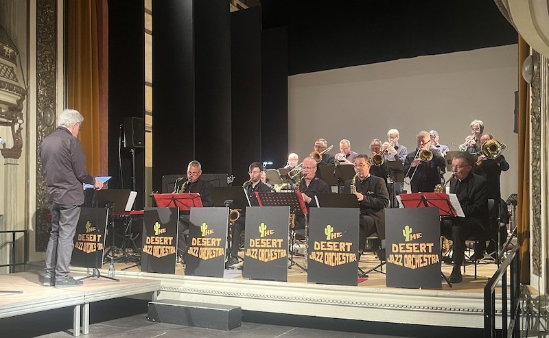 Das Desert Jazz Orchestra spielt auf einer Bühne unter der Leitung eines Dirigenten. Die Musiker tragen schwarze Kleidung und spielen Blasinstrumente., © Touristik Bad Wildbad GmbH Das Desert Jazz Orchestra spielt auf einer Bühne unter der Leitung eines Dirigenten. Die Musiker tragen schwarze Kleidung und spielen Blasinstrumente., © Touristik Bad Wildbad GmbH