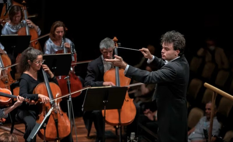 Ein Dirigent führt ein Orchester mit Streichinstrumenten auf einer Bühne. Die Musiker konzentrieren sich auf ihre Instrumente., © Kammerkonzerte Schwäbisch Hall e.V.