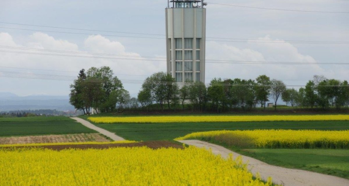 Ein Turm ragt über gelbe Rapsfelder und grüne Wiesen, umgeben von Bäumen, unter einem bewölkten Himmel., © Natur.Nah. Schönbuch & Heckengäu Ein Turm ragt über gelbe Rapsfelder und grüne Wiesen, umgeben von Bäumen, unter einem bewölkten Himmel., © Natur.Nah. Schönbuch & Heckengäu