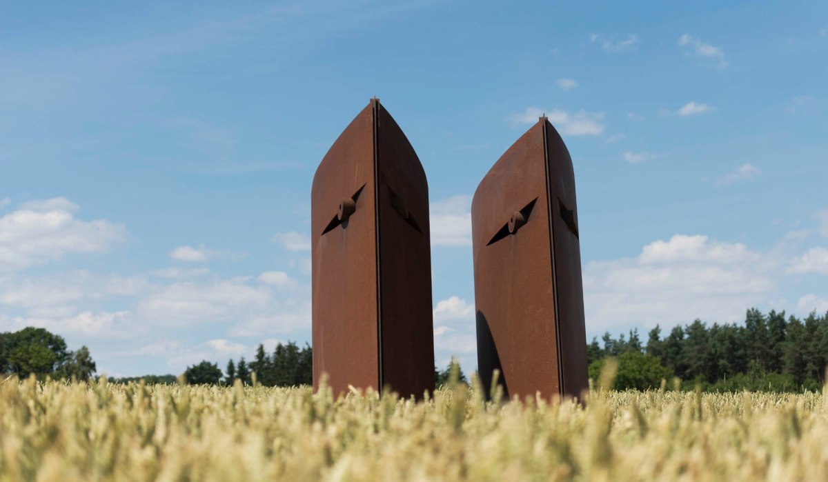 Zwei rostige, abstrakte Skulpturen stehen in einem Feld unter blauem Himmel. Im Hintergrund sind Bäume zu sehen., © Natur.Nah. Schönbuch & Heckengäu Zwei rostige, abstrakte Skulpturen stehen in einem Feld unter blauem Himmel. Im Hintergrund sind Bäume zu sehen., © Natur.Nah. Schönbuch & Heckengäu