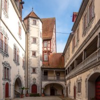 gepflasterter Schlossinnenhof, umgeben von hell verputzten Gebäuden mit grauer Illusionsmalerei umd Fenster und Türen, auf der rechten Bildseite eine offene Galerie im ersten Obergeschoss des Gebäudes, © Stadt Gaildorf